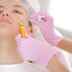 A woman receiving a cosmetic procedure with golden roller and syringe in a clinic.